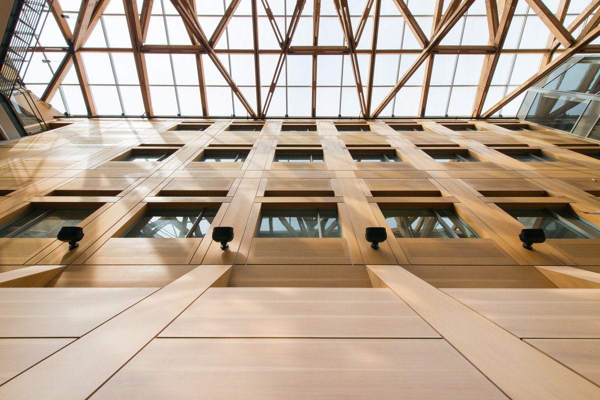 从UBC森林科学中心多层中庭向上看，室内白天的景色有装饰性的木镶板垂直表面，以及复杂的大质量木材支撑桁架和上面的玻璃屋顶
