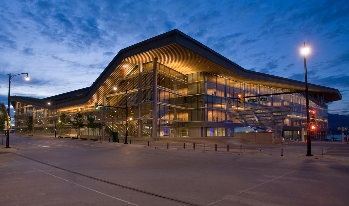 温哥华会议中心西大楼的现代玻璃和木材立面的外部夜景，展示了巨大的木质屋顶结构，顶部是加拿大最大的“活屋顶”，有40万株本土植物和草，以及四个蜂巢