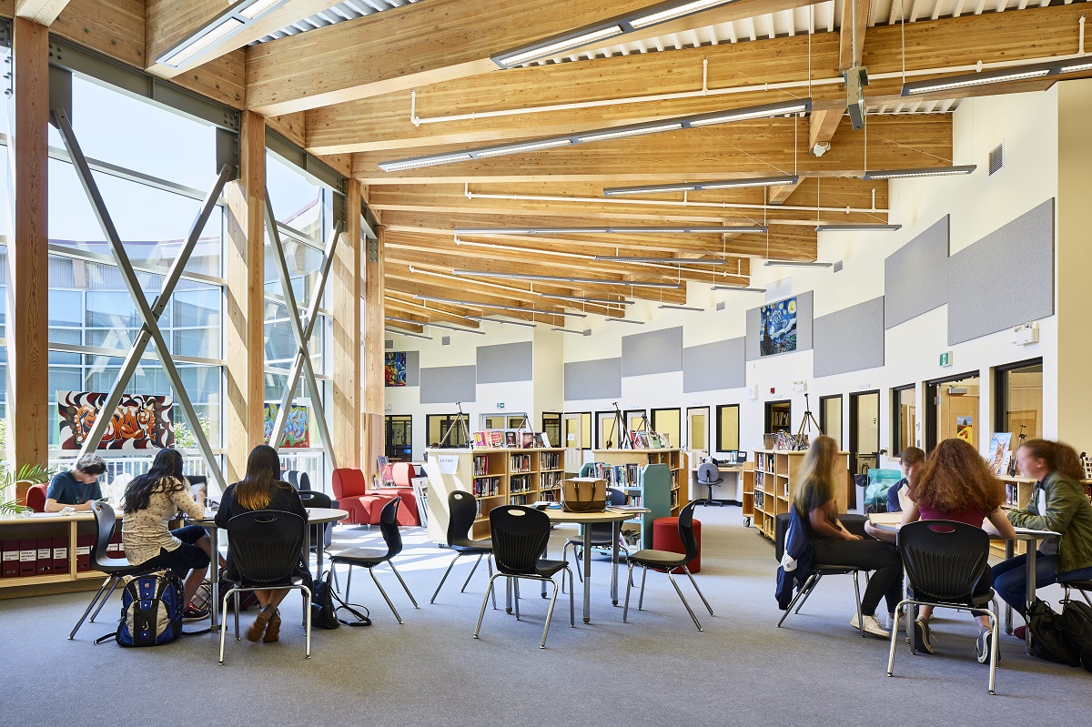 低层惠灵顿中学的内部白天视图，展示圆形开放图书馆和研究区，学生们坐在桌子旁，胶合层压木材(胶合木)“辐条”向外辐射