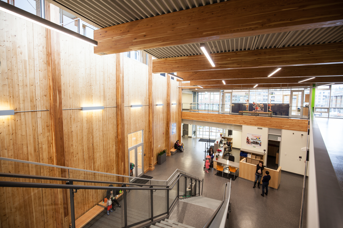 Wesbrook社区中心的多层低层主入口和中庭的室内日间楼梯图像显示交叉层压木(CLT)墙板和全跨度水平胶合木(胶合木)天花板梁