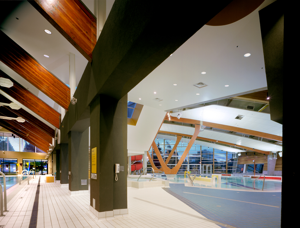 西温哥华水上运动中心低层主泳池的室内日间景观，拍摄自环形泳池和家庭泳池之间的中央柱子，并显示拱形胶合木(胶合木)支撑