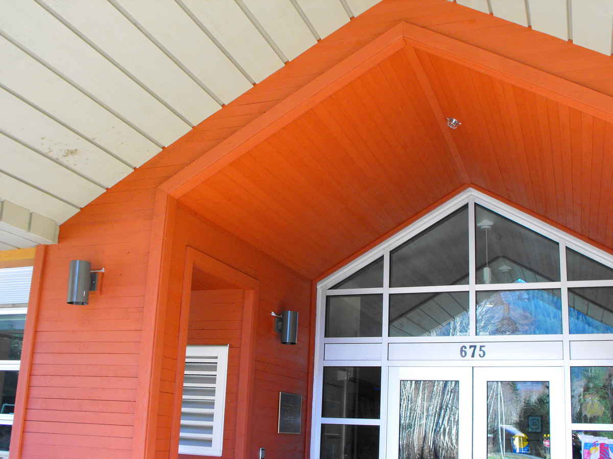 Zeballos小学/中学主入口的外部白天图像显示了外部木板镶板，包括亮橙色的色调