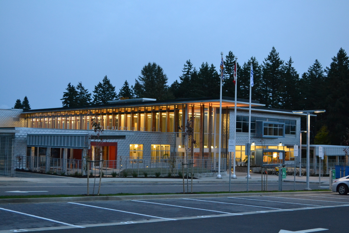 低层混合建筑École au - ceure -de-l ' île小学大楼正面和两层主入口的外部夜景，展示了由实锯重木材支撑的交叉叠层木材(CLT)板延伸的屋顶悬垂